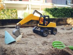 a yellow toy bulldozer digging in the sand